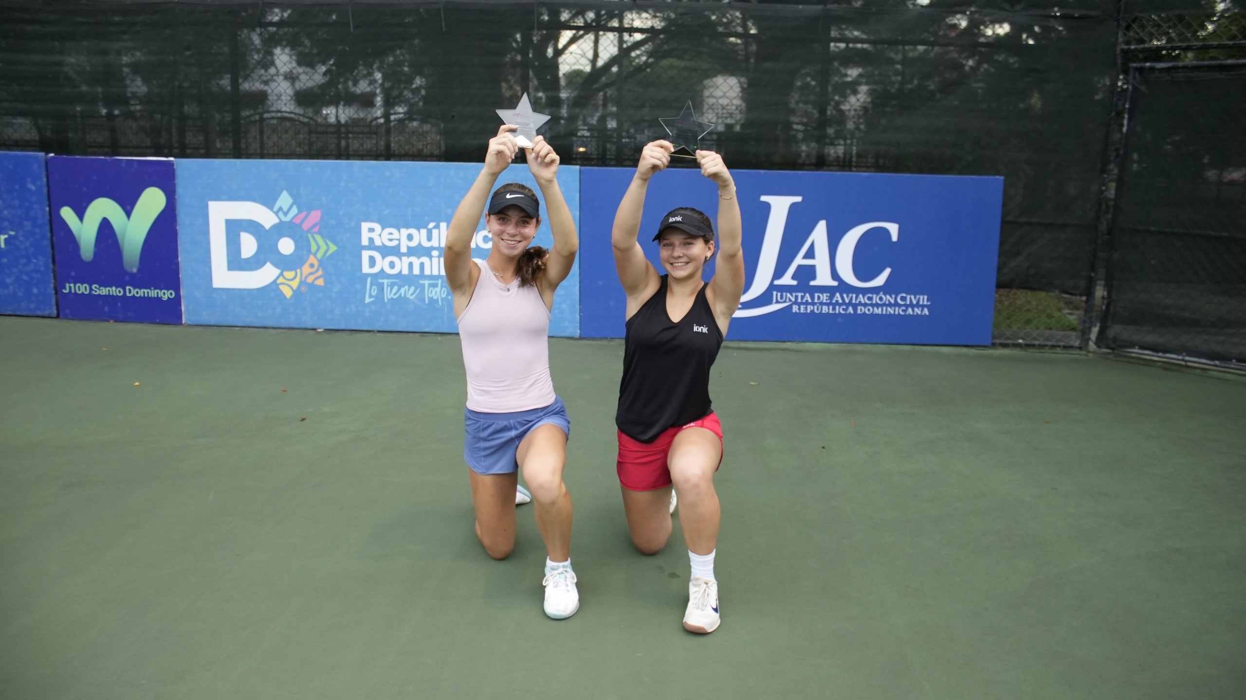 Adelie Osher y la canadiense Eve Thibault, muestran sus trofeos de campeones de dobles en la Copa Trinitaria.